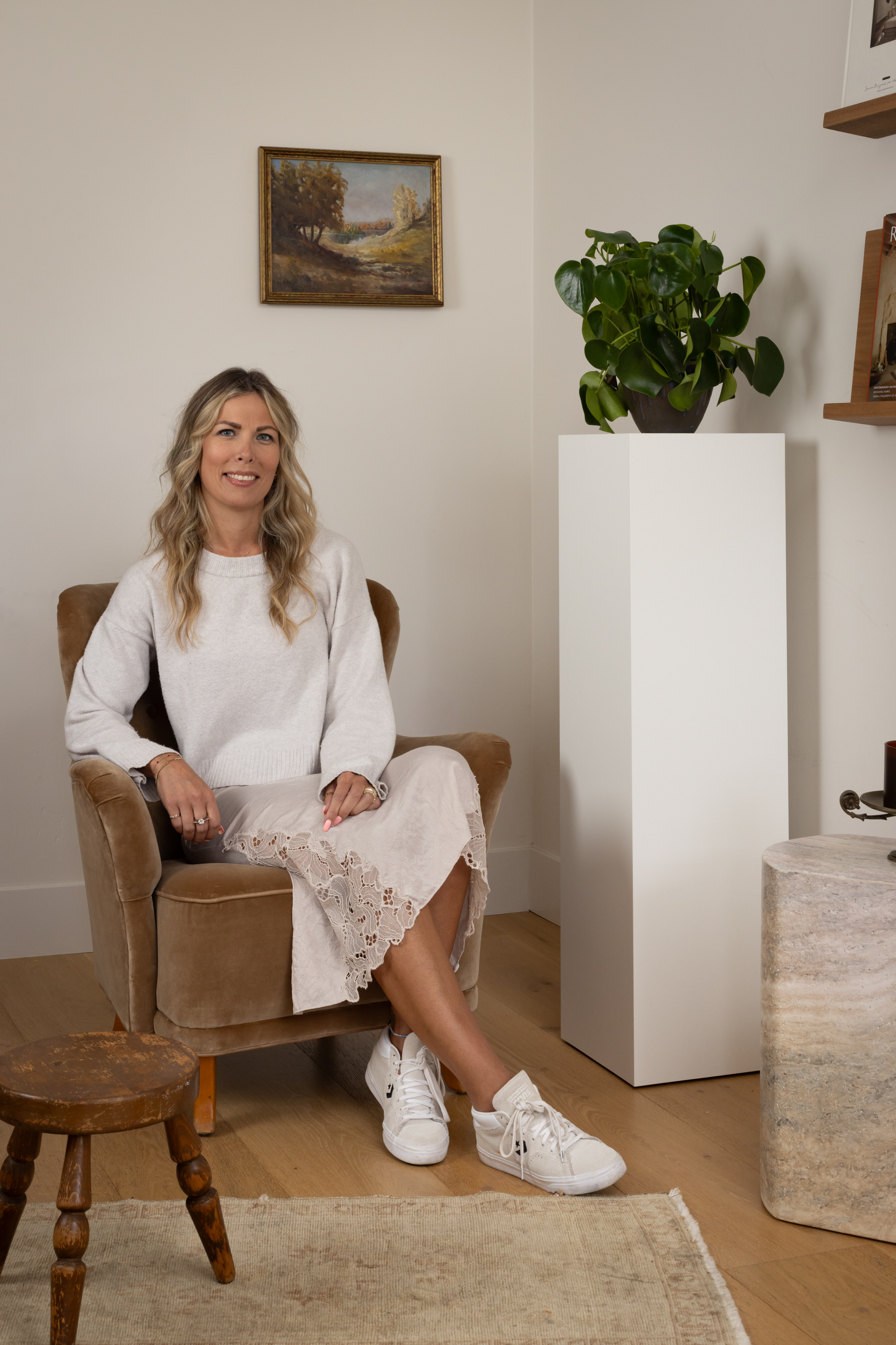 Woman sitting on a brown armchair in a modern interior with plants and artwork.