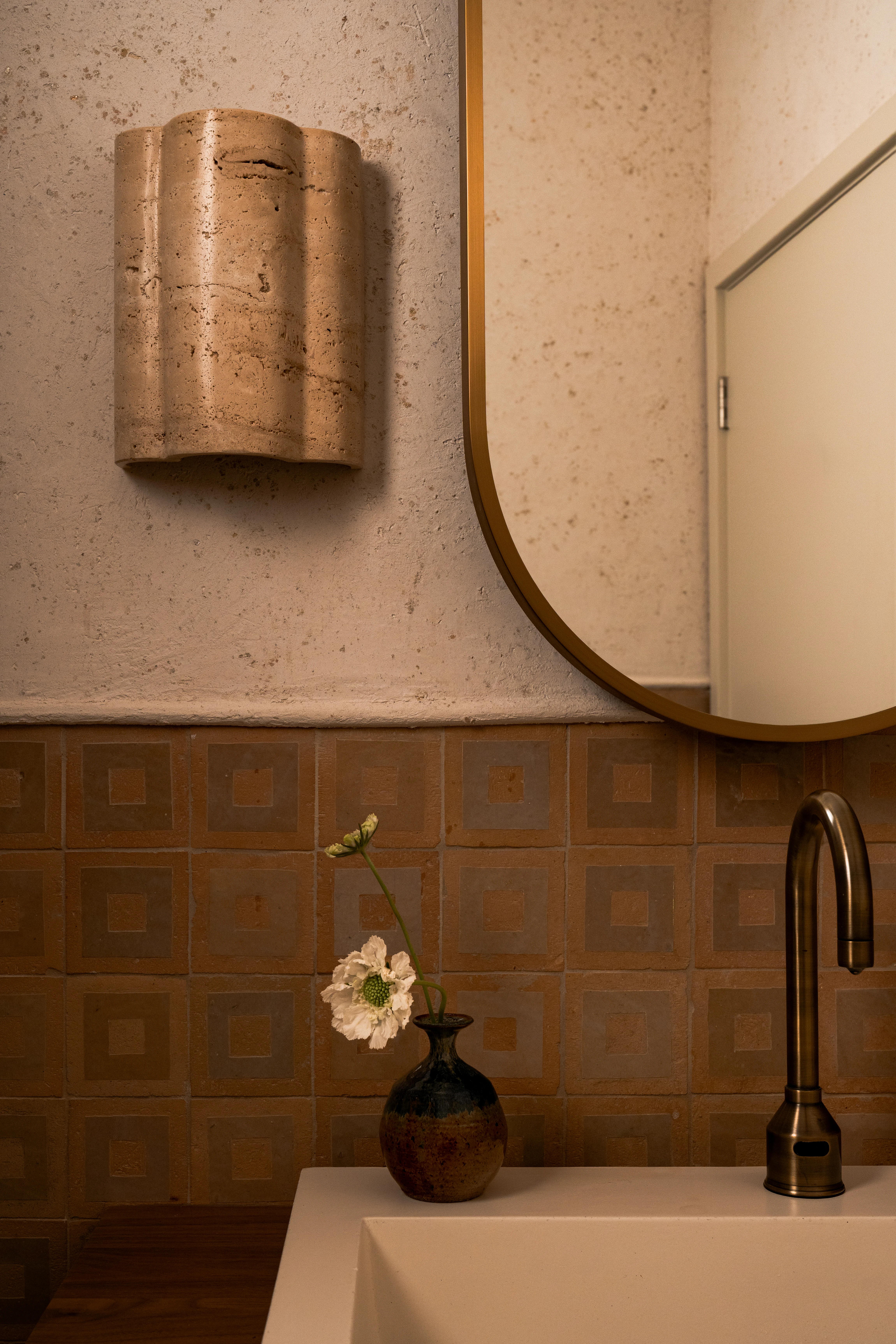 Sculptural sink and wall sconce in a terra-cotta powder room.