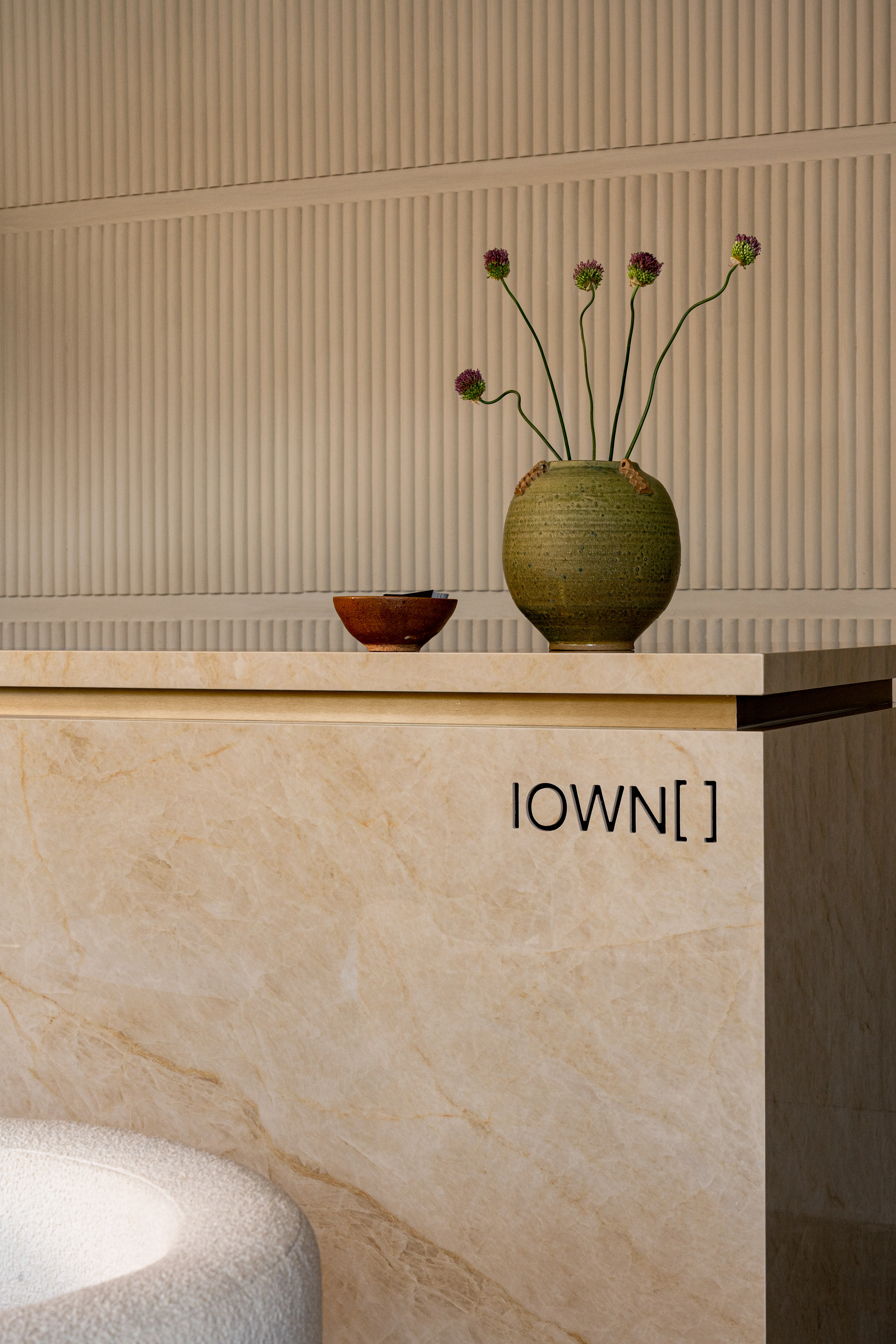 Stone reception desk with a vase and fluted wall detail.