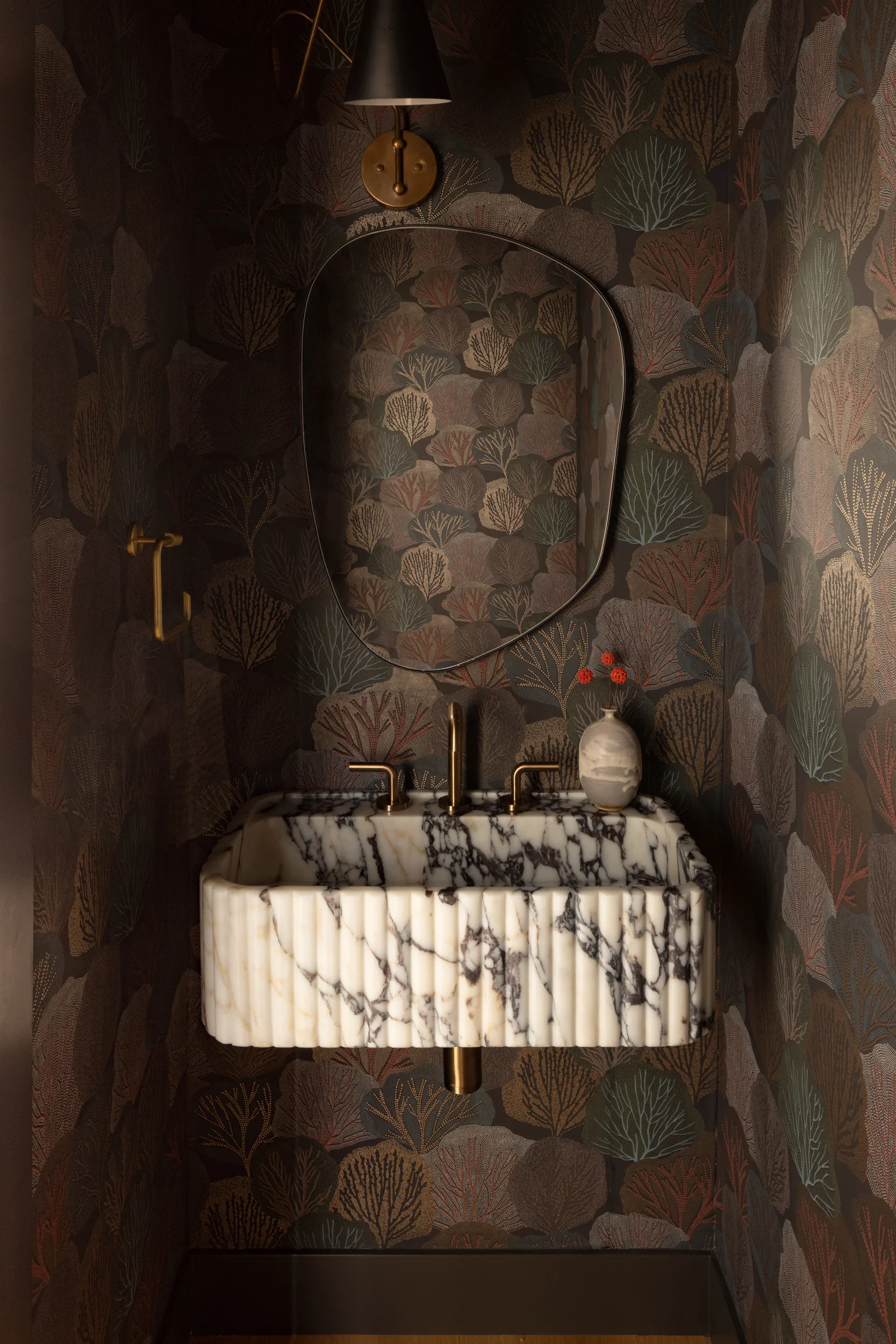 Powder room with a fluted marble wall sink, organic brass-framed mirror, and moody botanical wallpaper.