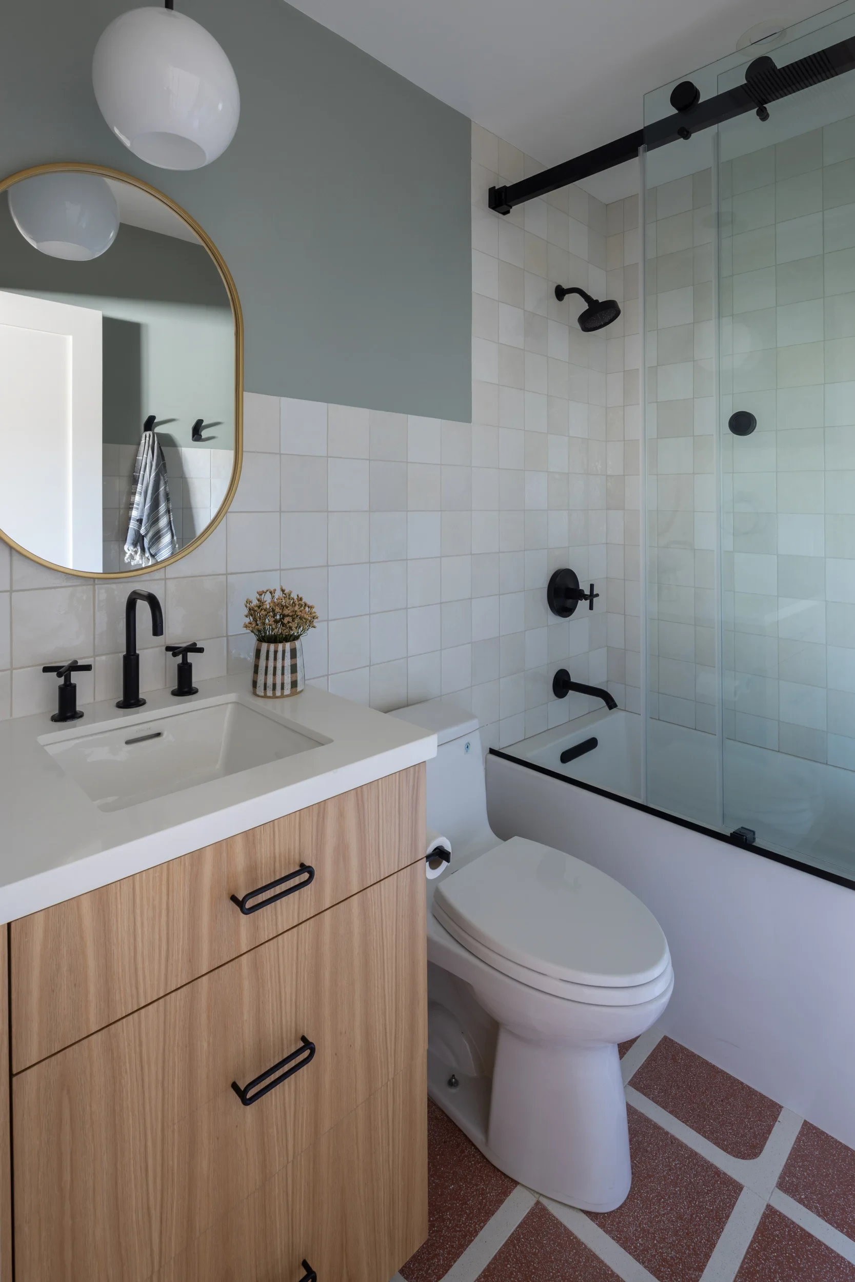 Guest bathroom with a white oak vanity, handmade white tile, and patterned terracotta floor.