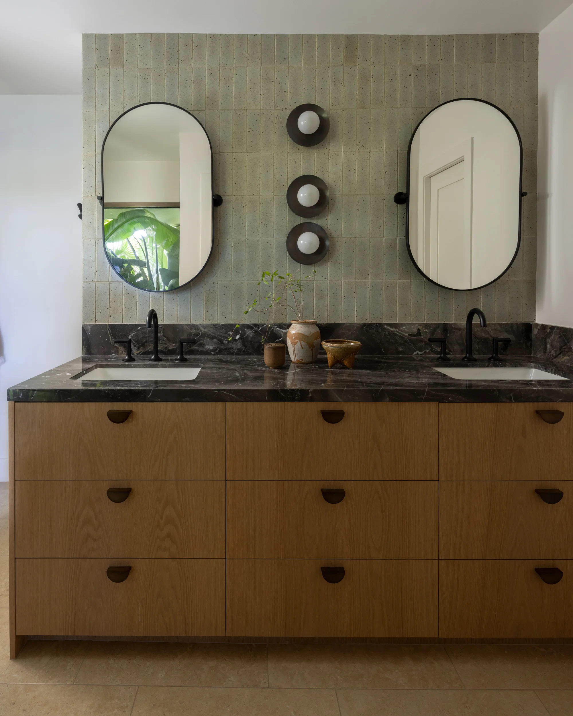 Primary bathroom double vanity with white oak drawers, dark stone counter, and black pill mirrors.