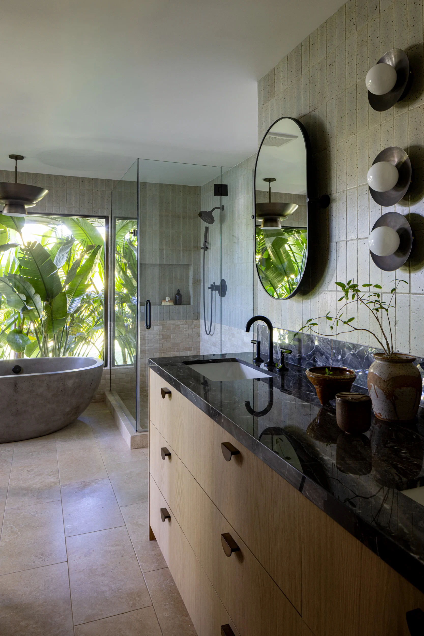 Primary bathroom vanity and stone soaking tub framed by lush tropical garden views.