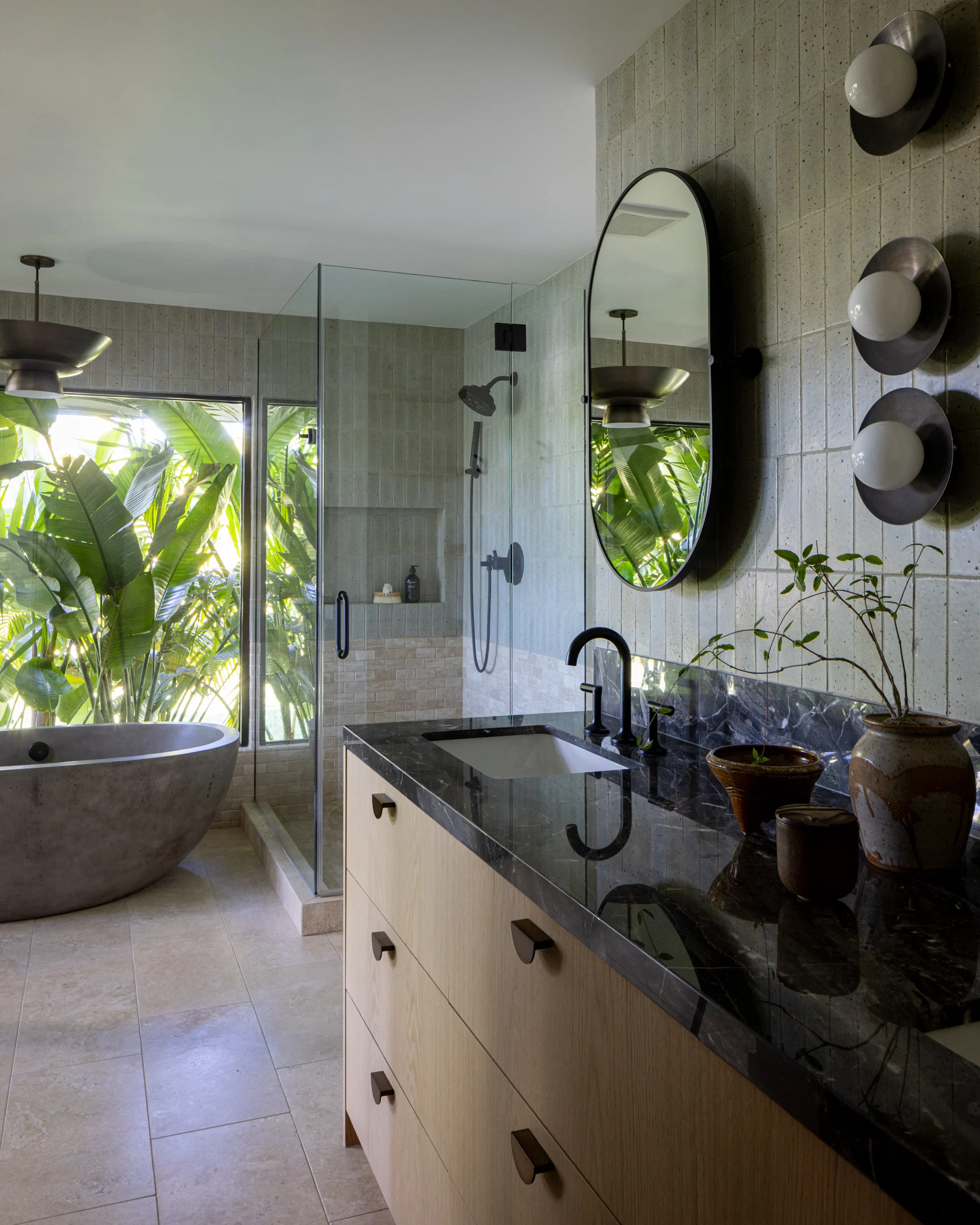 Primary bathroom with stone-topped oak vanity, sculptural sconces, and a garden-facing soaking tub.