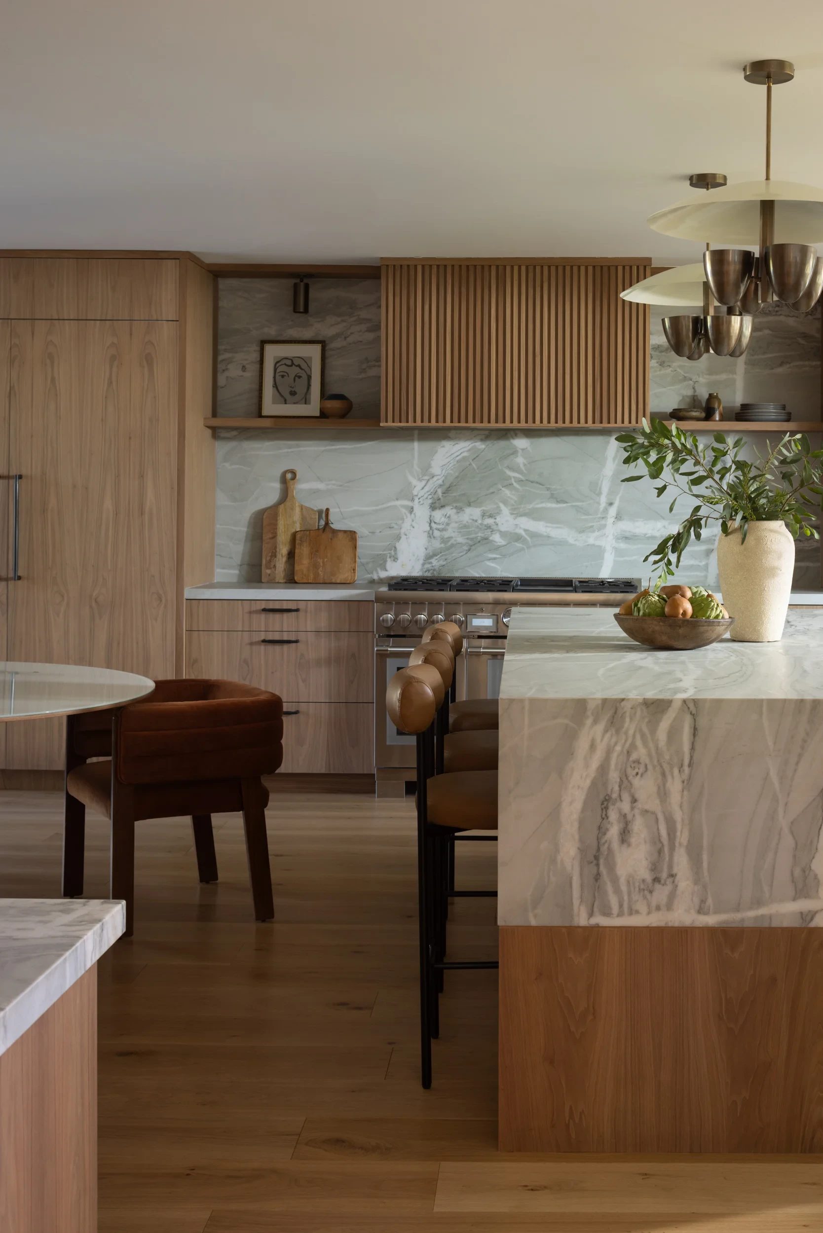 Kitchen island with a quartzite waterfall edge, walnut cabinetry, and leather counter stools.