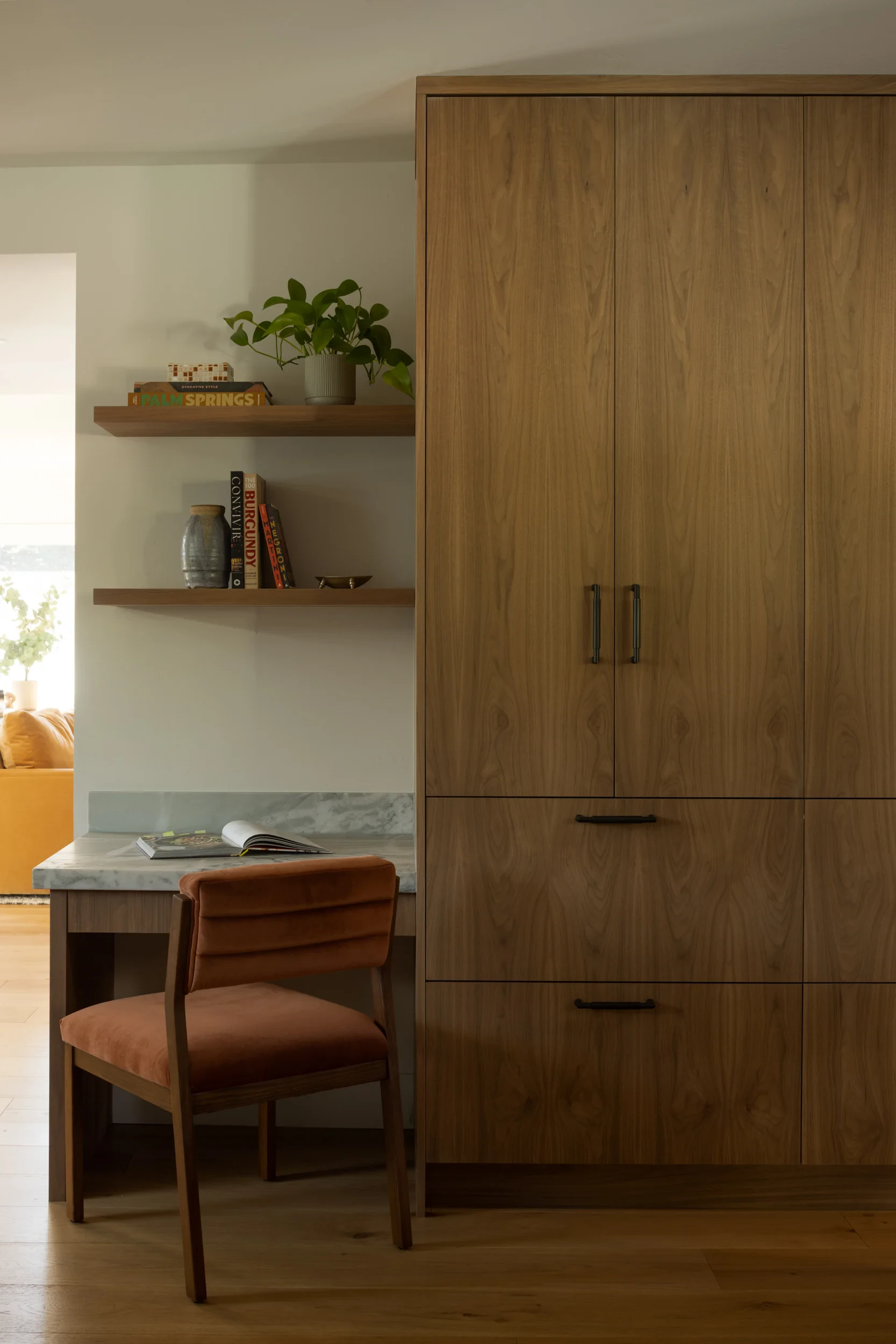 Built-in desk nook beside tall walnut pantry cabinetry and open shelves.